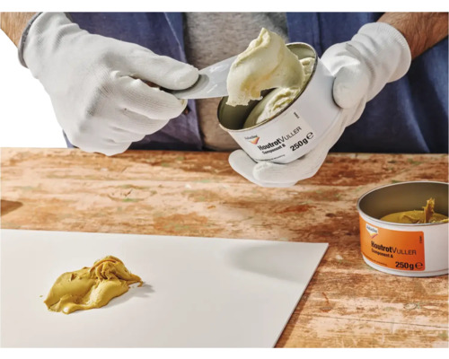 Houtreparatieplamuur wordt met een spatel uit een blik gehaald