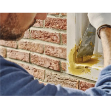 Een persoon gebruikt plamuur om een raamkozijnvoeg op een bakstenen muur af te dichten.