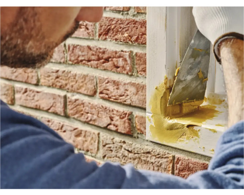 Een persoon gebruikt plamuur om een raamkozijnvoeg op een bakstenen muur af te dichten.