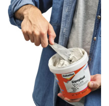 Persoon neemt gipsplaatvuller met een plamuurmes uit een bak.