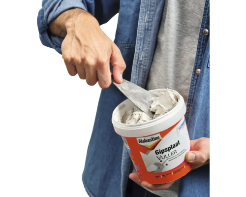 Persoon neemt gipsplaatvuller met een plamuurmes uit een bak.