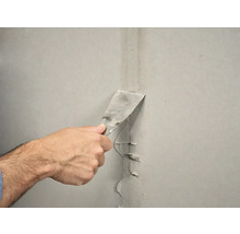 Een hand gebruikt een plamuurmes om een muur af te dichten.