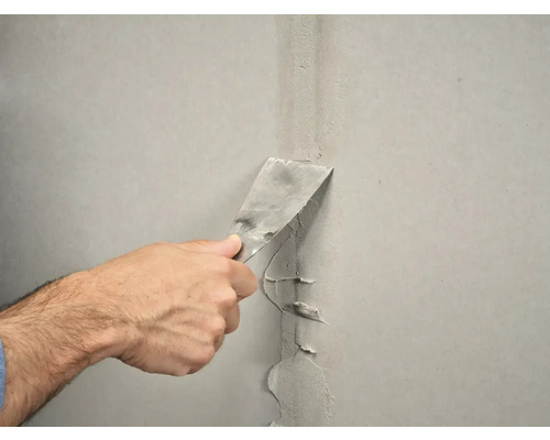 Een hand gebruikt een plamuurmes om een muur af te dichten.