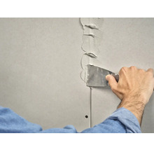 Iemand vult een gipsplaatvoeg met een plamuurmes.