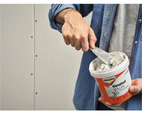 Man neemt plamuur uit een emmer Alabastine gipsplaatvuller.