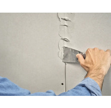 Iemand vult een gipsplaatnaad met een plamuurmes.