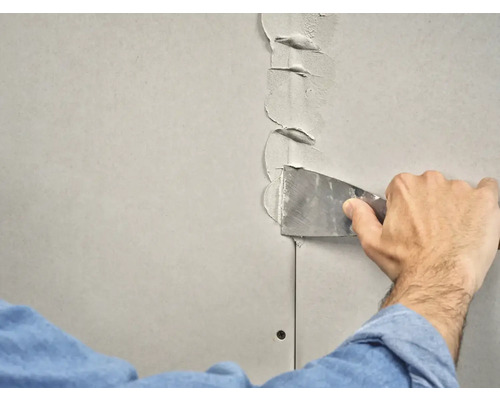 Iemand vult een gipsplaatnaad met een plamuurmes.