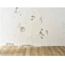 Muur met schade en reparaties op houten vloer