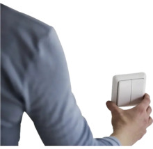 Een hand bedient een dubbele lichtschakelaar.