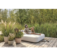 Man ontspant op een tuinligbed op een houten terras, omgeven door grassen en planten in plantenbakken.