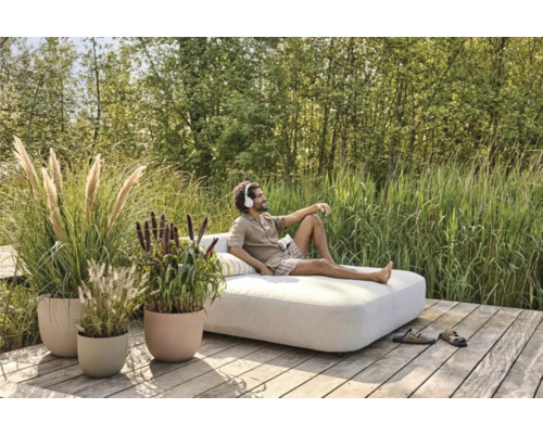 Man ontspant op een tuinligbed op een houten terras, omgeven door grassen en planten in plantenbakken.