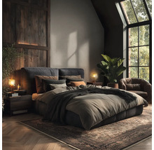 Slaapkamer met tweepersoonsbed, nachtkastjes, lampen, fauteuil, kamerplant en vloerkleed.