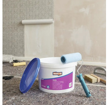 Scene met een emmer vliesbehanglijm, een verfroller, een behangborstel en een begonnen behang aan de muur