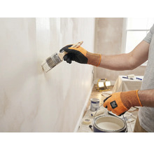 Een persoon schildert een muur met een kwast in een heldere ruimte.