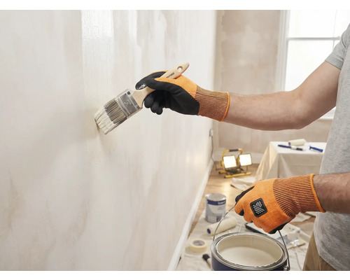 Een persoon schildert een muur met een kwast in een heldere ruimte.