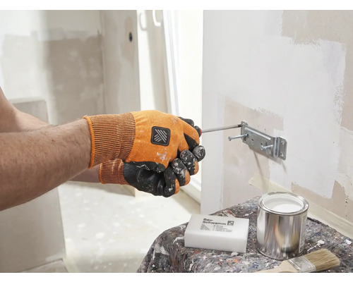 Een persoon bevestigt met een schroevendraaier een beugel aan een muur. Op een tafel staan een spons, een blik en een penseel.