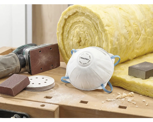 Scène met stofmasker, schuurpapier, schuurmachine en isolatiewol op een werkbank.