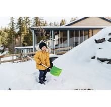 Een kind met een sneeuwschuiver in de besneeuwde tuin van een huis