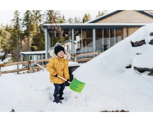 Een kind met een sneeuwschuiver in de besneeuwde tuin van een huis
