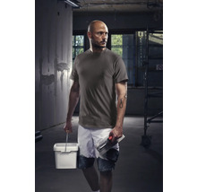 Vakman met T-shirt, korte broek, emmer en troffel op een bouwplaats.