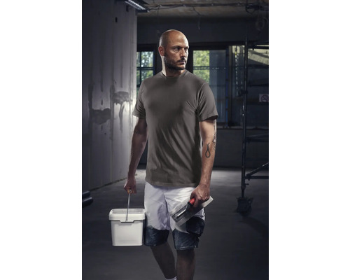 Vakman met T-shirt, korte broek, emmer en troffel op een bouwplaats.