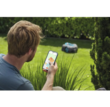 Man bedient gazonmaaierrobot via smartphone in de tuin