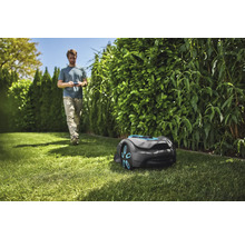 Scene met een robotmaaier op een gazon en een persoon op de achtergrond.