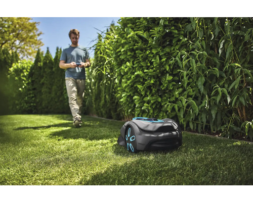 Scene met een robotmaaier op een gazon en een persoon op de achtergrond.