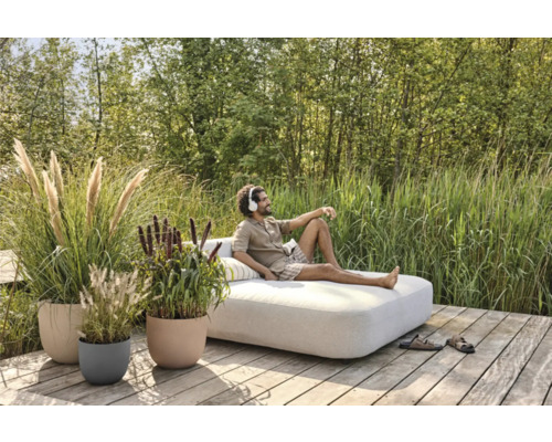 Scene met man die ontspant op een buitenshuis sofa, omringd door planten in bloempotten op een houten terras