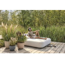 Tuinscène met een man die op een loungesofa ligt, omringd door siergrassen in plantenbakken.