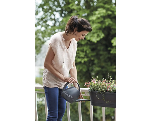 Vrouw geeft planten water in een bloembak met een gieter op een balkon.