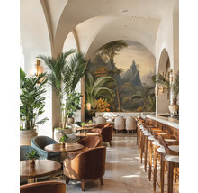 Heldere barruimte met booggewelven, tropische muurschildering, houten meubels, fluwelen fauteuils en grote kamerpalmen.