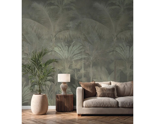 Vliesbehang met palmenpatroon in een lichte woonkamer achter een crèmekleurige bank, een tafellamp en een grote kamerplant.