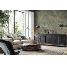 Moderne woonkamer met lichte bank, leren poef en vliesbehang met palmenmotief op de wand achter een dressoir.