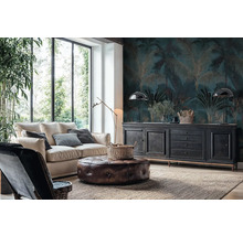 Woonkamer met fotobehang met palmenpatroon in donkerblauw en goud, een lichte bank, leren poef en zwart dressoir voor grote ramen.