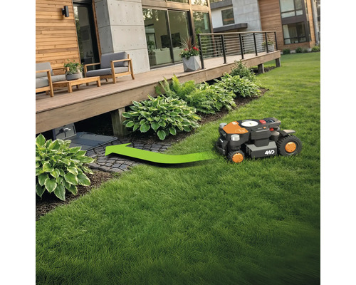 Een robotmaaier rijdt op een gazon naar zijn laadstation onder een houten terras.