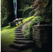 Scene met een robotmaaier op een groen gazon naast een stenen trap