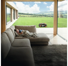 Jongen slaapt op de bank terwijl de robotmaaier in de tuin werkt