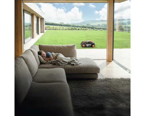 Jongen slaapt op de bank terwijl de robotmaaier in de tuin werkt