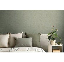 Moderne slaapkamer met kussens in groen en crème voor een gestructureerde olijfgroene muur en een Anthurium plant.