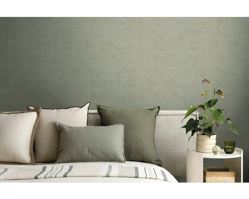 Moderne slaapkamer met kussens in groen en crème voor een gestructureerde olijfgroene muur en een Anthurium plant.