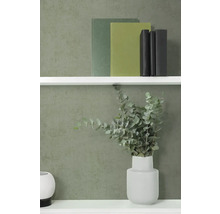 Vliesbehang met fijne structuur in donkergroen op een muur achter een witte wandplank met boeken en een vaas met eucalyptus.