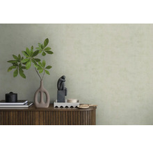 Behang met structuur in lichtgroen achter een houten dressoir met vaas, takken en een beeldje in een minimalistisch interieur.