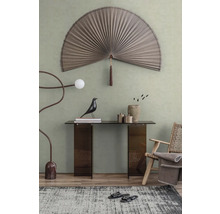 Modern interieur met een grote decoratieve wandwaaier, glazen sidetable, houten fauteuil en artistieke vloerlamp voor een groene muur.