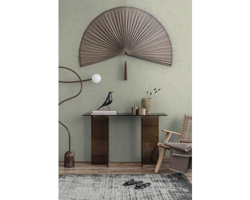 Modern interieur met een grote decoratieve wandwaaier, glazen sidetable, houten fauteuil en artistieke vloerlamp voor een groene muur.