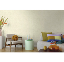 Woonkamer met behang met textuur, houten fauteuil met knoopkussen, bijzettafel en bank met kleurrijke kussens op een parketvloer.