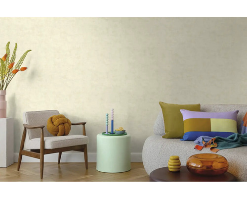 Woonkamer met behang met textuur, houten fauteuil met knoopkussen, bijzettafel en bank met kleurrijke kussens op een parketvloer.