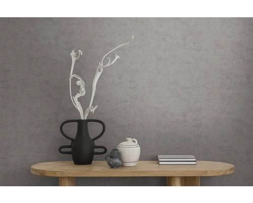 Wand met gestructureerd behang met betonlook achter een houten consoletafel met zwarte en witte keramische vazen en droge takken.