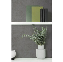Vliesbehang in antraciet met betonlook en fijne structuur, gecombineerd met een witte wandplank, boeken en een vaas met eucalyptus.