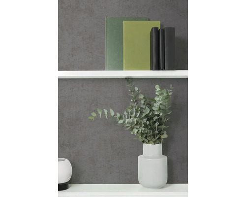 Vliesbehang in antraciet met betonlook en fijne structuur, gecombineerd met een witte wandplank, boeken en een vaas met eucalyptus.
